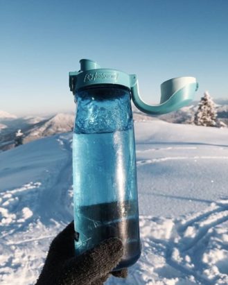 24oz OTF Bottle Blue with Glacial Cap held on top of a snowy mountain