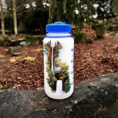32 oz. Ultralite Wide-Mouth bottle with Blue cap sitting on top of a rock in the woods