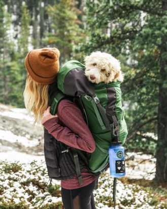 Hiker in the woods with small dog in backpack and 32 oz. Wide Mouth bottle clipped to backpack strap