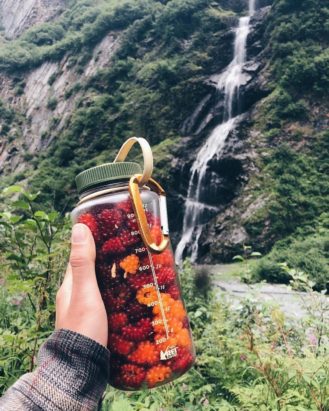 32 oz. Wide Mouth Bottle filled with raspberries being held in front of a waterfall