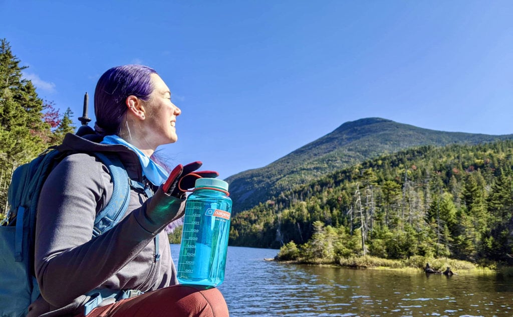 Hiker holding a Nalgene water bottle in front of a mountain lake
