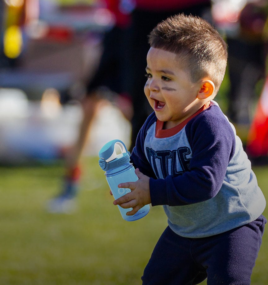 A little boy on a sports field holding a 12 oz OTF lock top bottle in blue