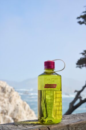 A 32oz NM Thrill in Motion water bottle sits on a wooden railing by the ocean.